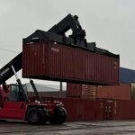 Червоний річстакер піднімає морський контейнер серед штабелів на складі