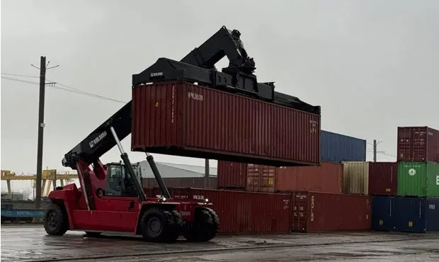 Червоний річстакер піднімає морський контейнер серед штабелів на складі