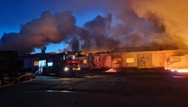 Пожежна машина біля палаючого складу вночі серед густого диму і полумя