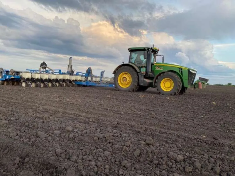 Зелений трактор John Deere тягне синю сівалку по сухому зораному полю