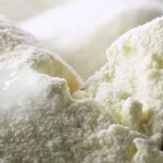 Струмінь молока ллють на гірку сухого молока поруч із дерев’яною лопаткою